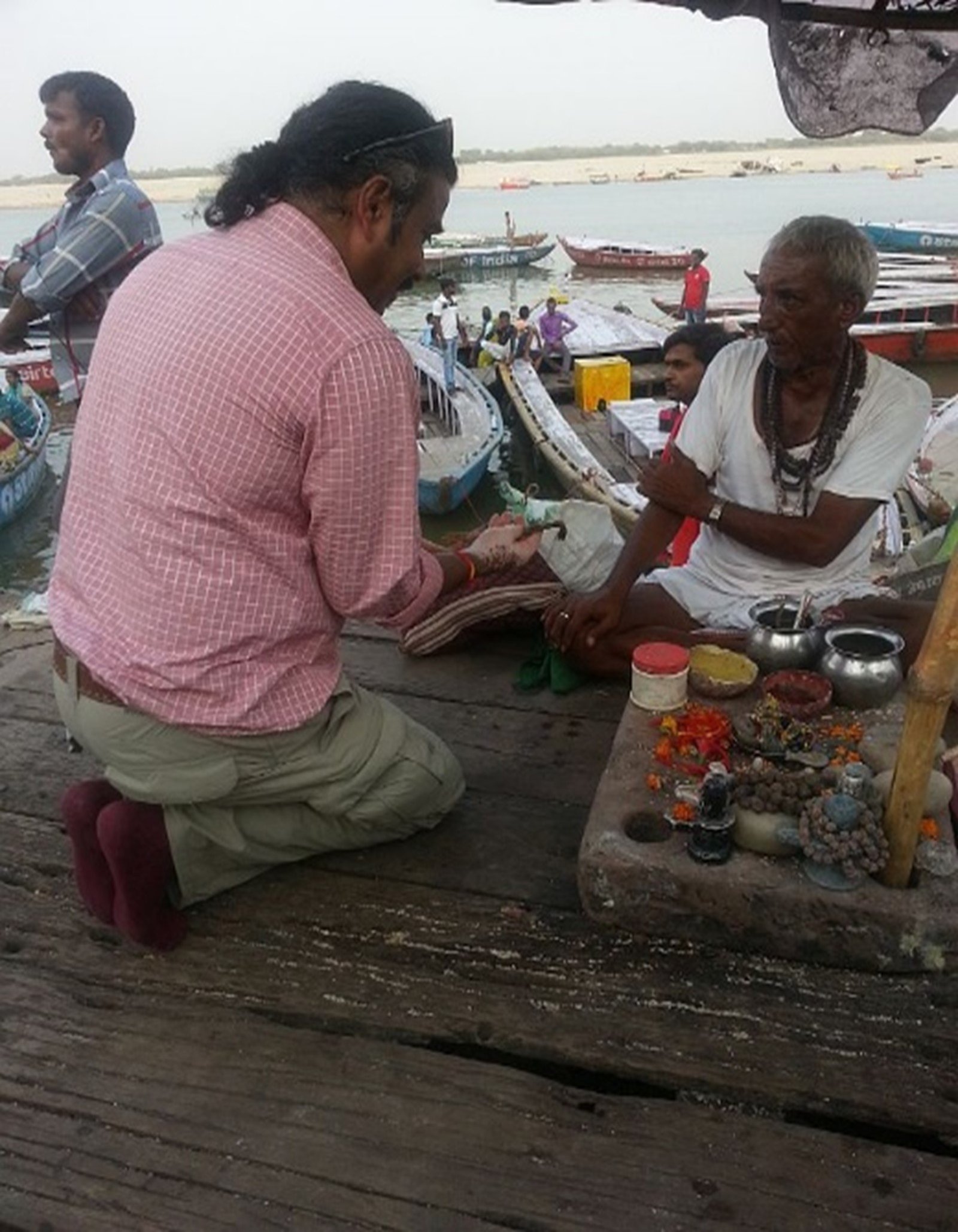 An kneeling tourist receives blessings from a sadhu or guide by the Ganges river bank in Varanasi, India.