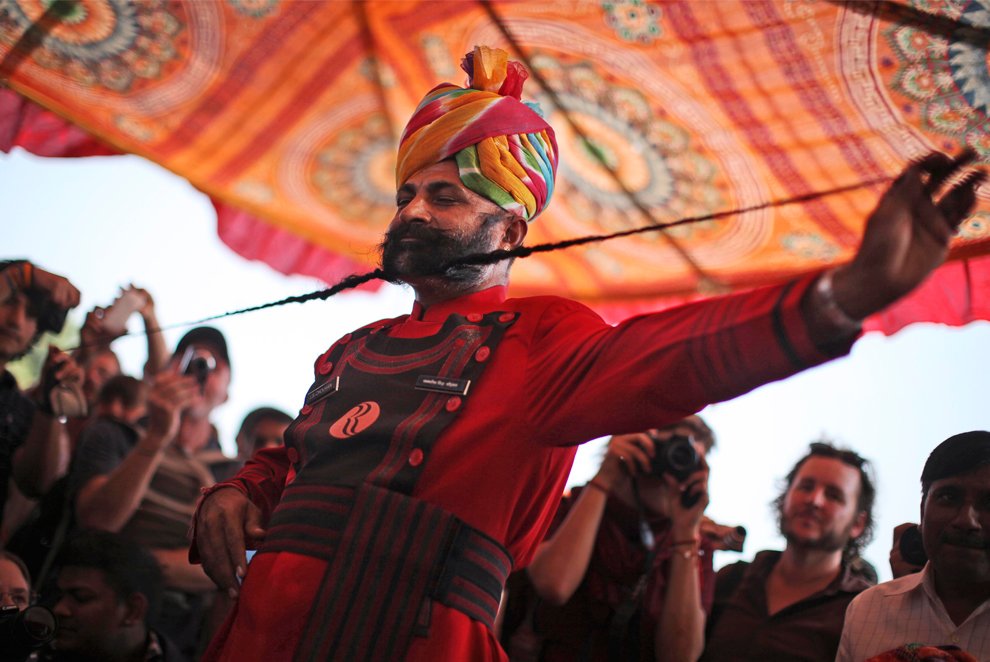 rajasthani performer with colorful turban demonstrating traditional mustache art during cultural event
