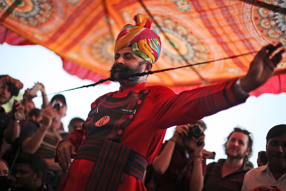rajasthani performer with colorful turban demonstrating traditional mustache art during cultural event