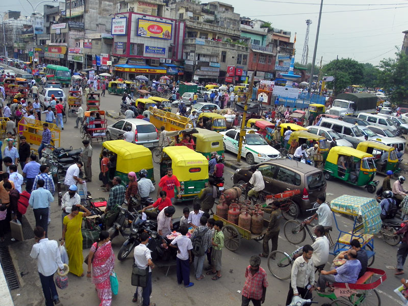 Crowded Indian city street with auto rickshaws, local market traffic, street vendors, and busy urban lifestyle
